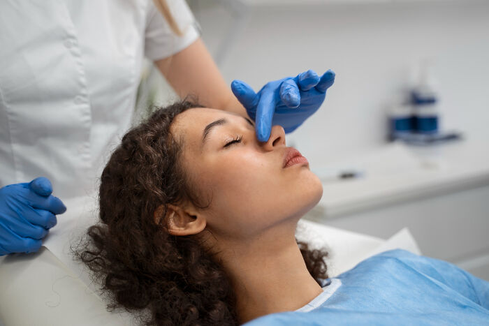 Patient relaxed in medical setting with healthcare worker adjusting nose, highlighting effects of anesthesia during treatment.