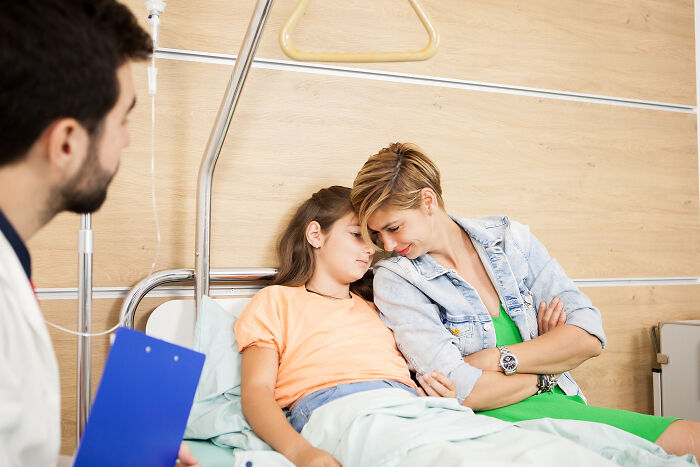 Young patient resting in hospital bed with worried family member nearby, during effects of anesthesia discussion.