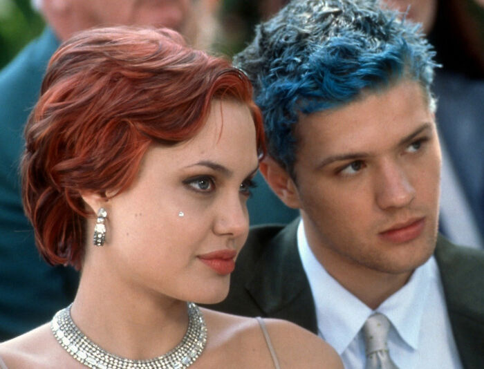 Young man with blue dyed hair and woman with red hair sitting closely, showcasing Knox bold new look style.