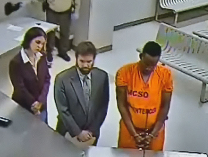 Man in orange prison jumpsuit with two people standing beside him in a courtroom after celebrity chef found guilty of family slaying.