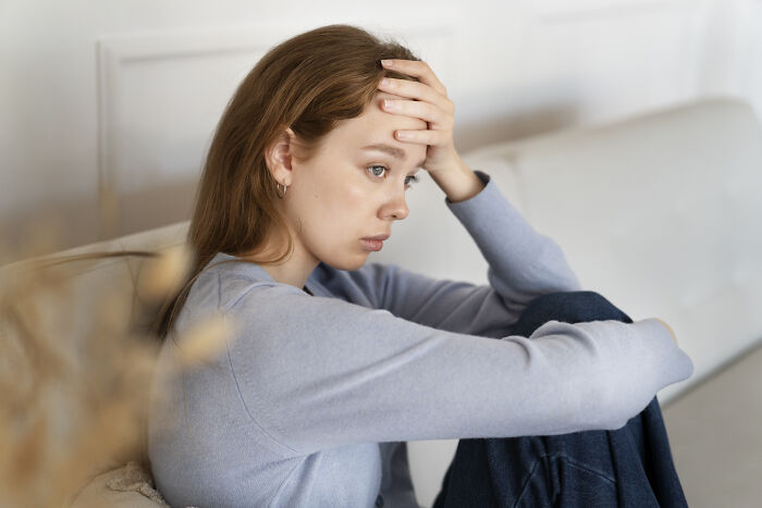 Young woman sitting on sofa looking stressed and regretful, reflecting on challenges of having kids.