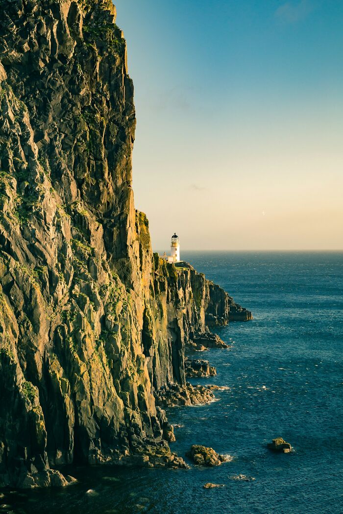Steep rocky cliffs with a lighthouse by the ocean capturing positive stereotypes about various countries.