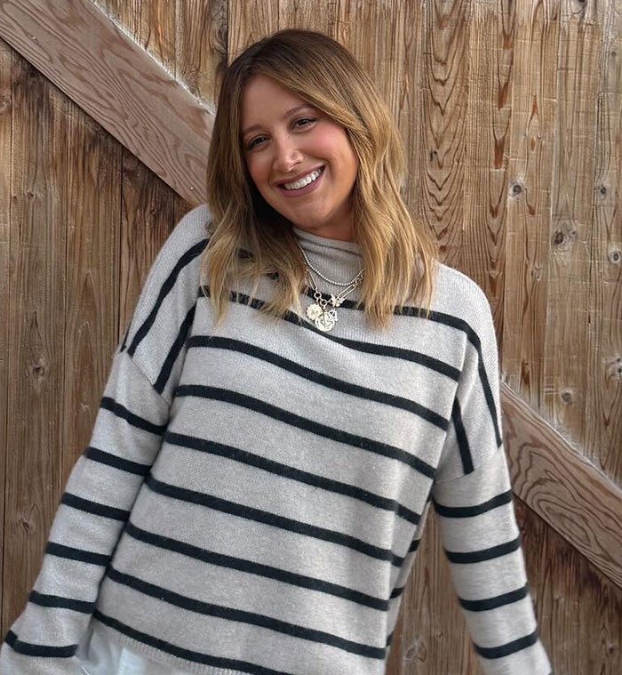 Ashley Tisdale smiling in a striped sweater, sharing details about her official name change and reasons behind it.