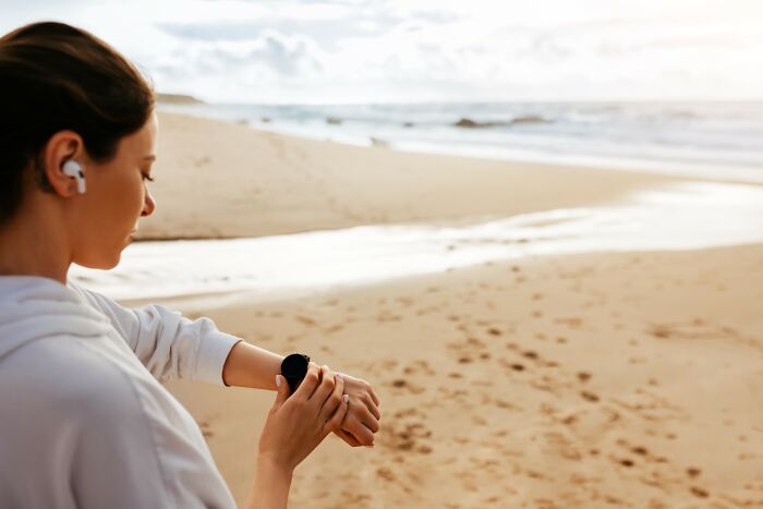 Woman wearing earbuds checking smartwatch on a beach, illustrating stories about the craziest coincidences experienced by people.