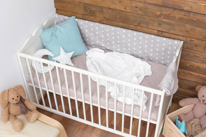 White baby crib with aunt crib storage, soft bedding, pillows, and stuffed toys in a cozy nursery corner.