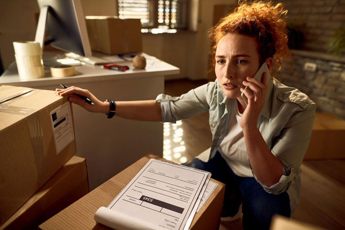 Woman organizing aunt crib storage baby items at home, talking on the phone while checking boxes and paperwork.