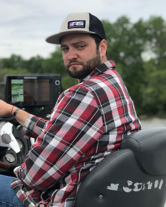 Man in a plaid shirt and cap looks back while sitting in a boat, related to autopsy revealing truth behind newlywed couple case.