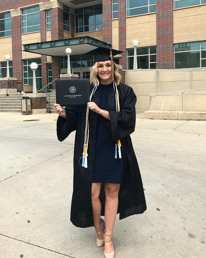 Young woman in graduation gown holding diploma outside a university building after newlywed couple found lifeless in their car