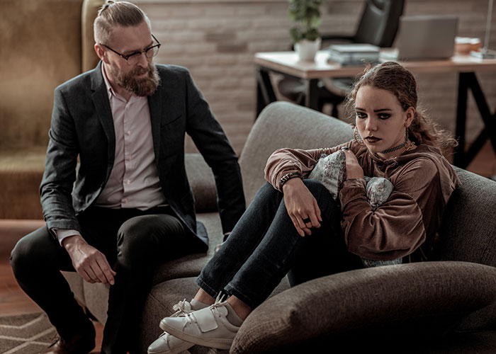 Man with glasses talking to upset teenage girl on couch illustrating wild family dramas and conflicts.