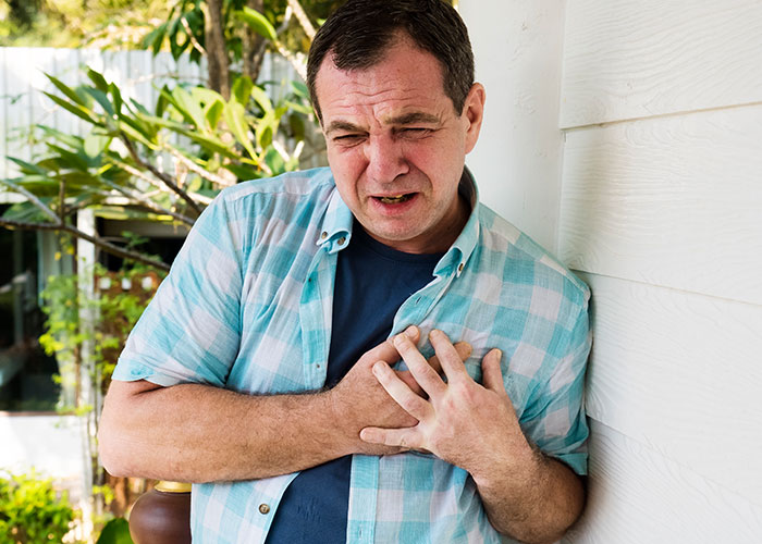 Middle-aged man clutching chest in pain outside a house illustrating wild family dramas and stressful family moments.