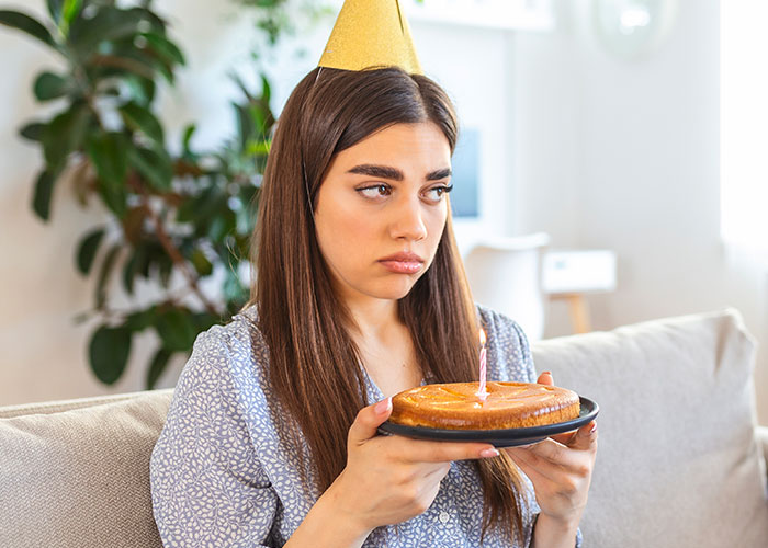 Young woman wearing a party hat looking sad while holding a birthday cake, illustrating wild family dramas.