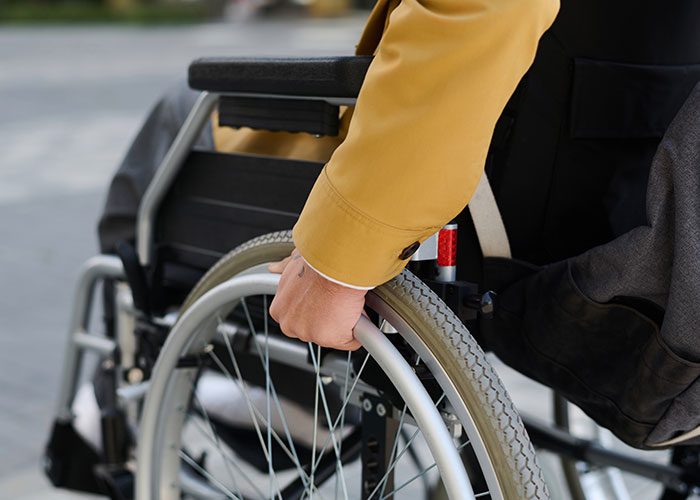 Person in a yellow jacket gripping a wheelchair wheel, highlighting moments that weren’t what they looked like in everyday life.