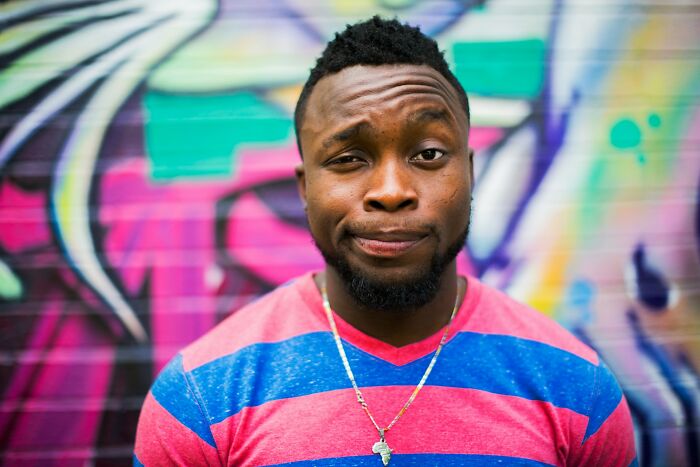 Man in a striped shirt expressing culture shock while visiting Australia in front of colorful urban graffiti wall.