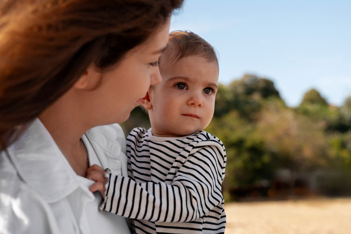 Woman at a theme park carrying an unknown baby, looking concerned as parents vanish into the crowd nearby.