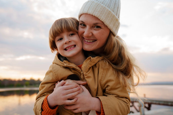 Woman smiling and hugging child outdoors by the water, illustrating a story about cheating and affair child disputes. Woman smiling and hugging child outdoors by the water, illustrating a story about cheating and affair child disputes.
