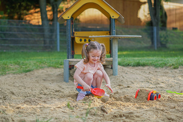Young girl playing in playground sandpit with toys, highlighting issues of bullying and gender discipline challenges.