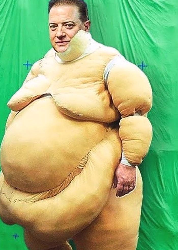 Man in an unhinged behind-the-scenes inflatable costume standing in front of a green screen, funny photo moment.