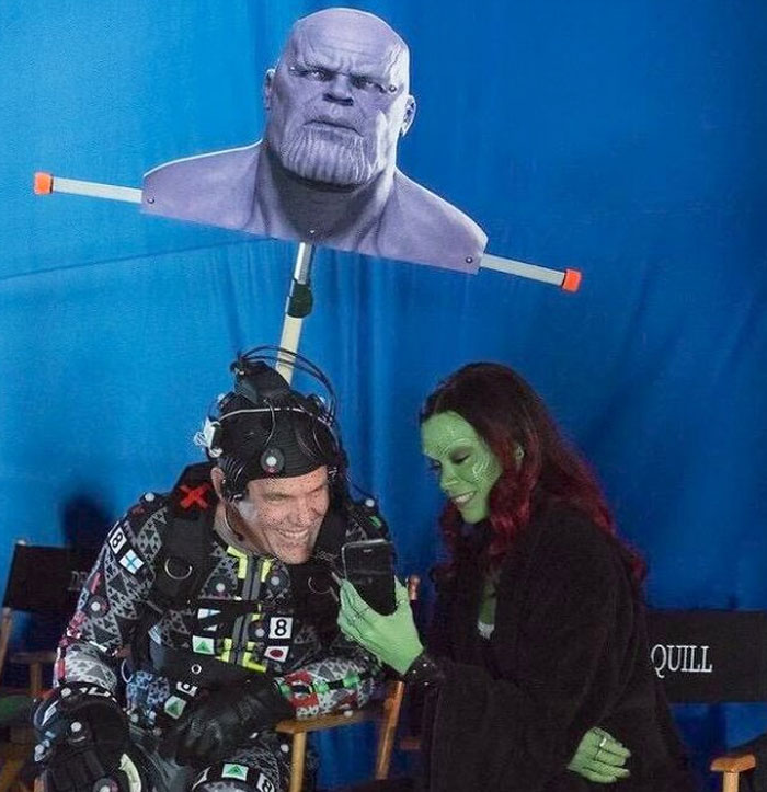 Actors on set in unhinged behind-the-scenes moment with motion capture gear and green screen background.