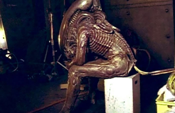 Alien creature costume sitting unhinged on a box behind the scenes, a moment captured for meme potential.