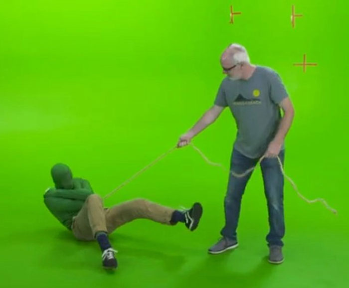 Behind-the-scenes photo showing two men on a green screen set, one pulling the other with a rope in a meme-ready moment.