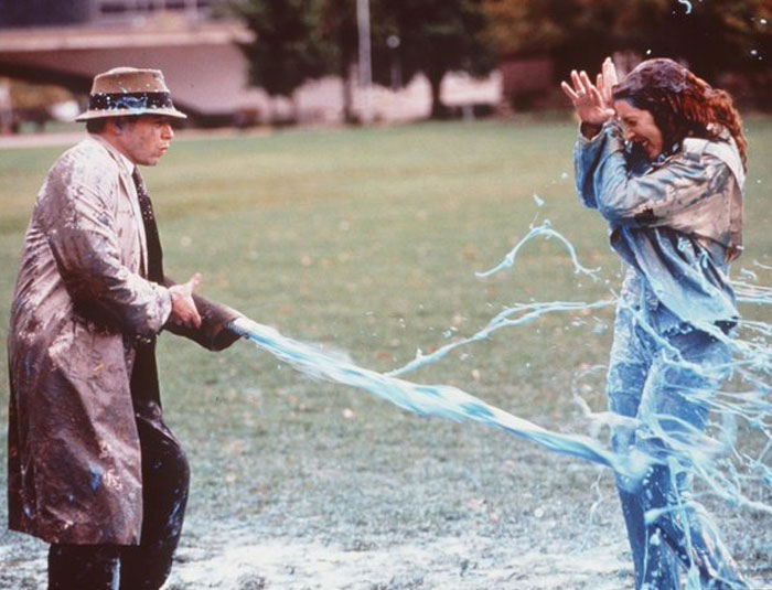 Man spraying woman with water from hose in a humorous unhinged behind-the-scenes photo causing a splash.