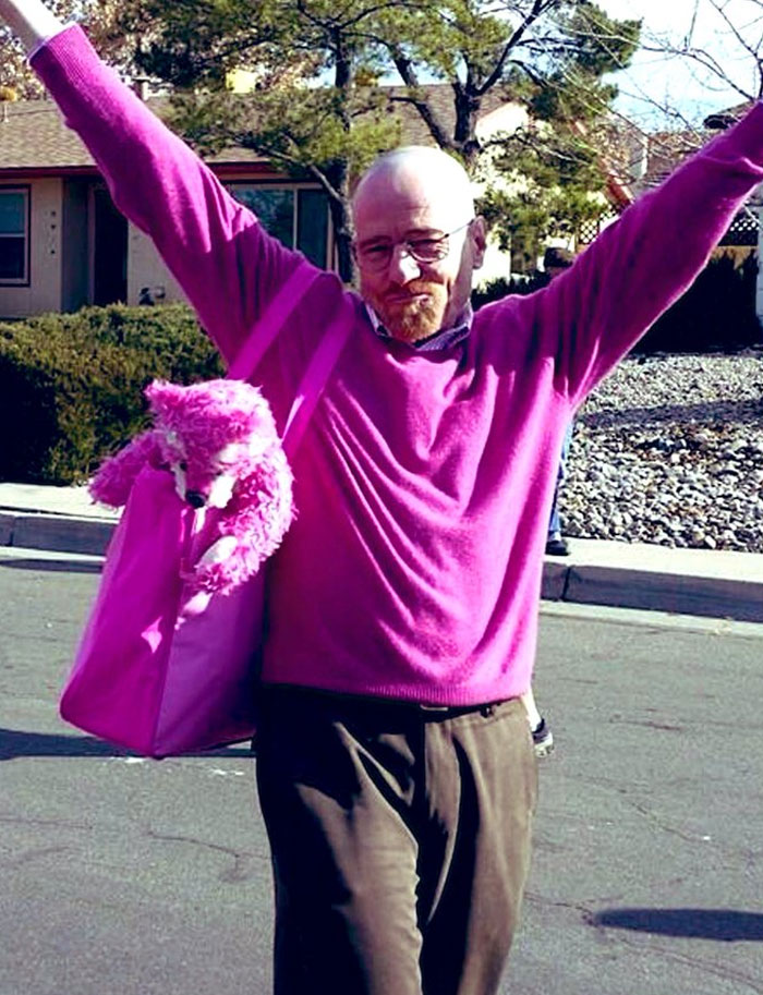 Man in bright pink sweater holding arms up and carrying matching pink bag with stuffed animal in unhinged behind-the-scenes photo.