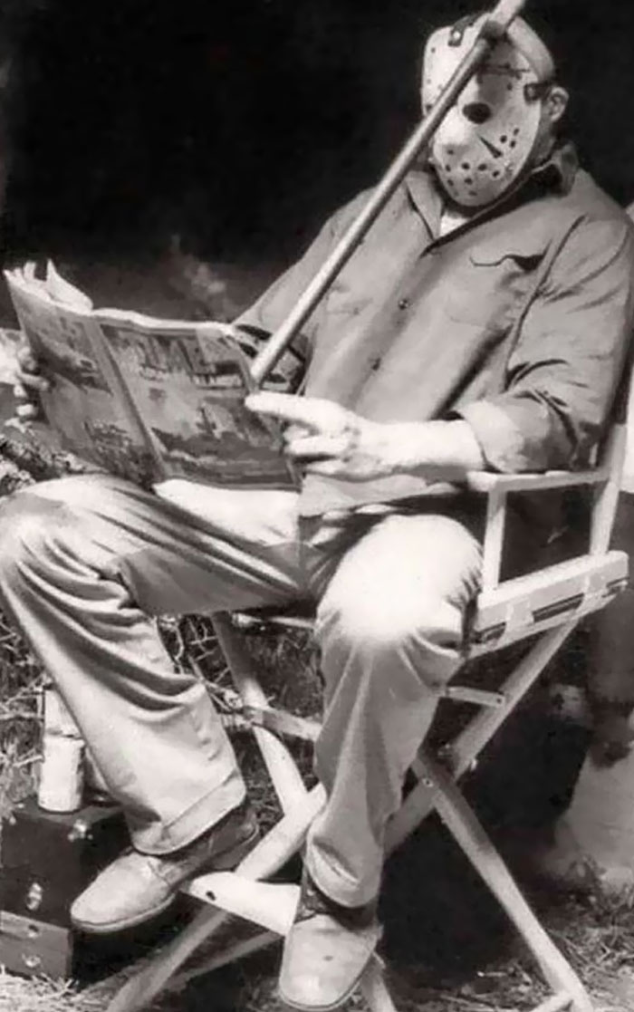 Black and white behind-the-scenes photo of a person in a hockey mask reading a magazine, a meme moment waiting to happen.