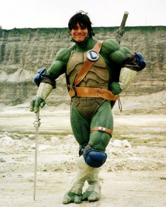 Behind-the-scenes photo of a man in a detailed Teenage Mutant Ninja Turtle costume posing outdoors, meme ready moment.