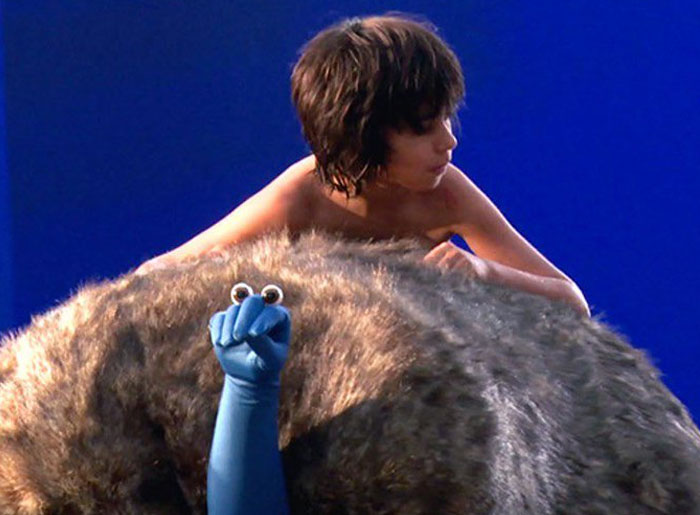 Behind-the-scenes photo showing a young actor with a furry creature and a blue-gloved hand with googly eyes.