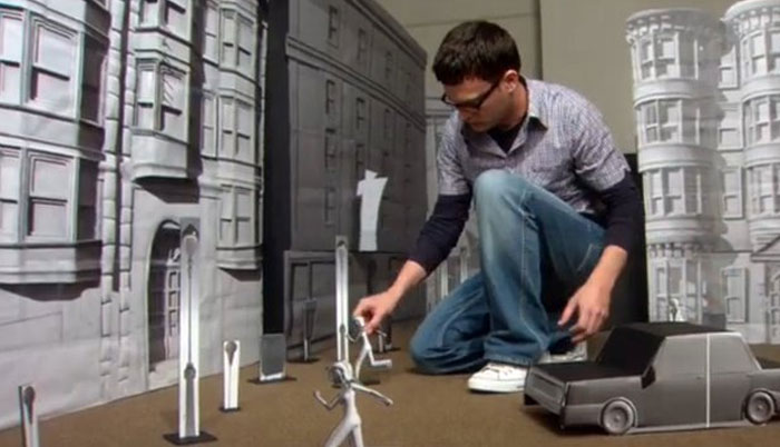 Man adjusting miniature figures and buildings in a behind-the-scenes setup for unhinged behind-the-scenes photos.