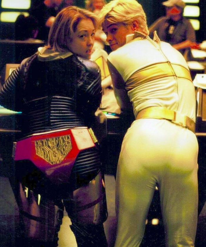 Behind-the-scenes photo showing two actors in futuristic costumes smiling at the camera on set, perfect for meme moments.