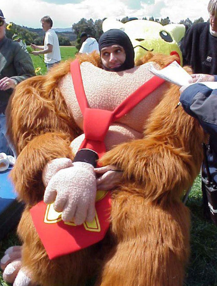 Person in an unhinged behind-the-scenes photoshoot wearing a large, humorous Donkey Kong costume outdoors with others around.