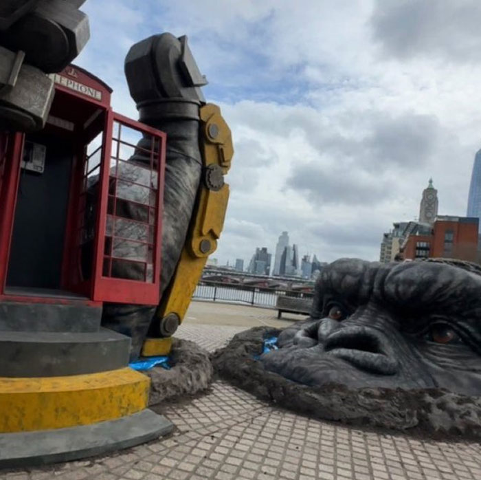 Giant gorilla head sculpture next to broken robotic arm and red phone booth in an unhinged behind-the-scenes photo.