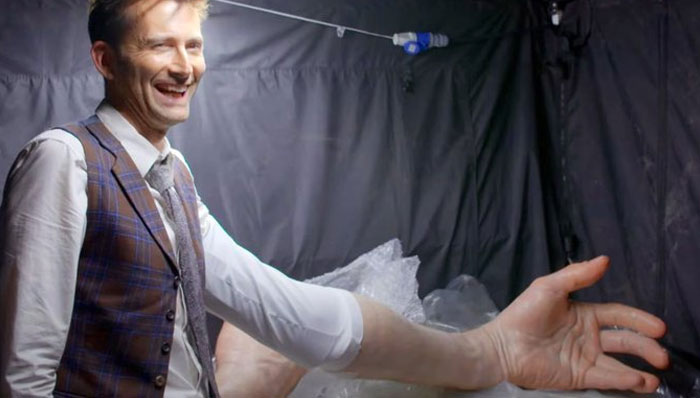 Man laughing behind the scenes with a giant fake arm prop, an unhinged behind-the-scenes photo moment.