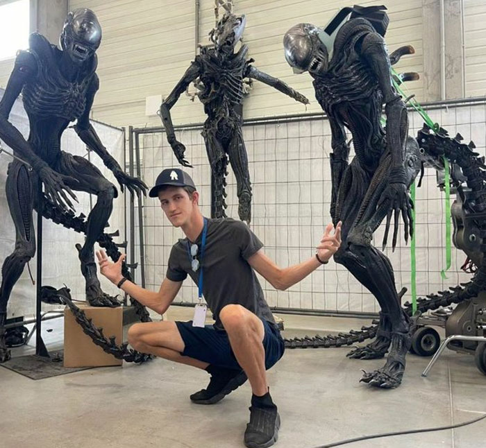 Person posing with unhinged behind-the-scenes alien costumes, creating funny and meme-worthy moments on set.