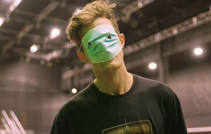 Man wearing a face mask over his eyes in a dimly lit behind-the-scenes setting, capturing unhinged moments for memes