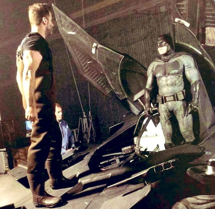 Behind-the-scenes photo of actors in Batman costumes on set with Batmobile, an unhinged moment caught on camera.