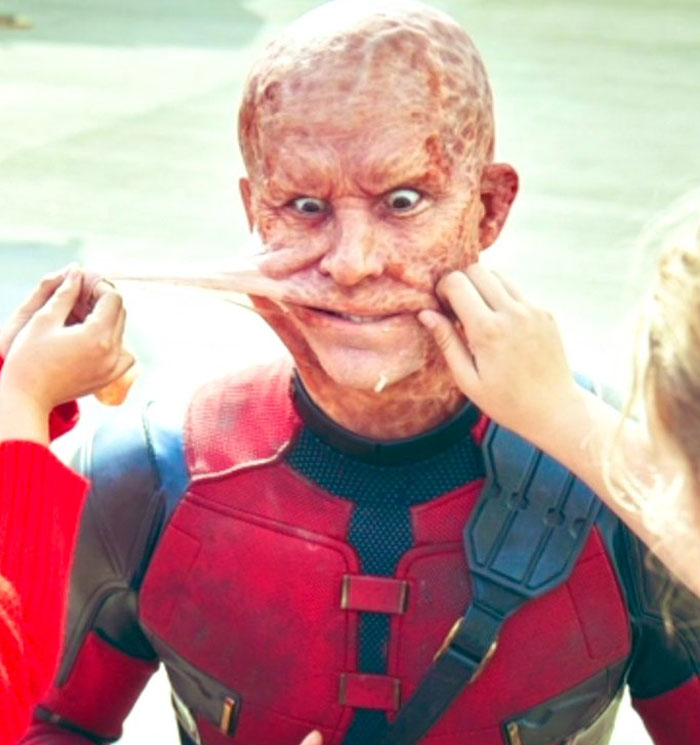 Actor in Deadpool costume with makeup being stretched by two people in an unhinged behind-the-scenes photo.