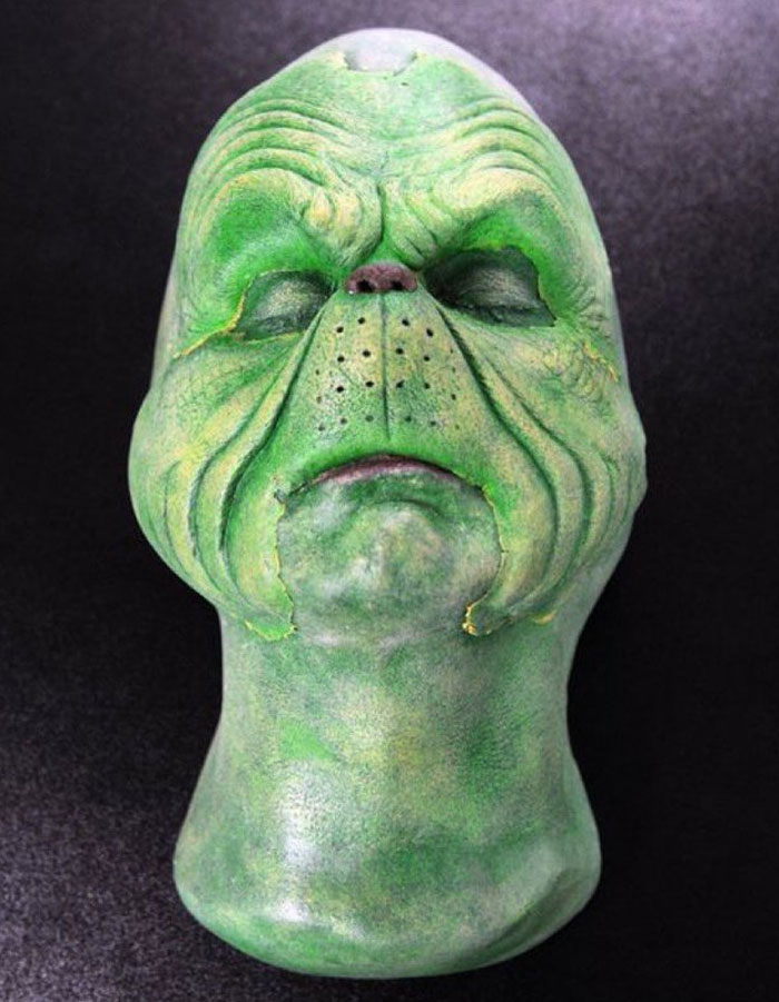 Unhinged behind-the-scenes photo of a person wearing detailed green alien makeup with closed eyes and textured skin.