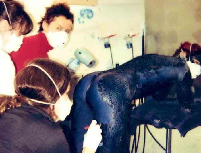 Behind-the-scenes photo showing costume artists painting a detailed bodysuit, an unhinged moment before filming.