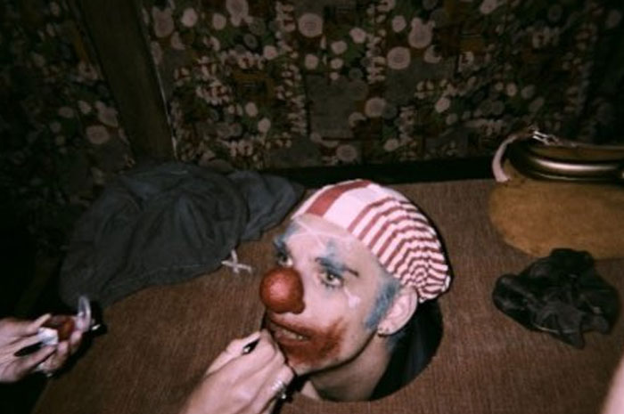 Actor with clown makeup and red nose seated at a table, captured in an unhinged behind-the-scenes photo moment.