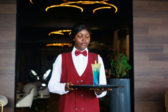 Young woman in uniform carrying a tray with a colorful drink, representing stories of golden child in families.
