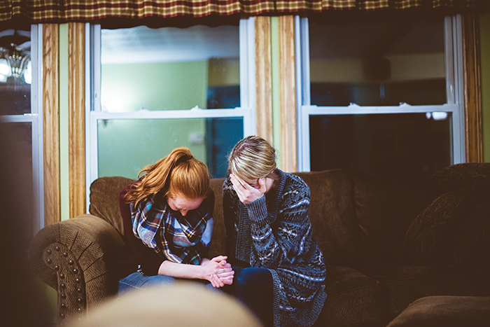 A teenage girl and her mother sitting on a couch looking upset, reflecting a parenting conflict about buying food.