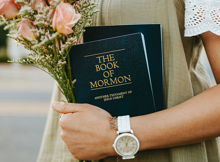 Person holding The Book of Mormon and a bouquet of flowers, symbolizing moments of truly lucky chances.