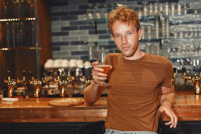 Young man at bar holding a beer glass, with polyamorous woman making a pass and a girlfriend confrontation implied