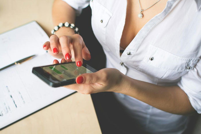 Person with red nail polish using smartphone for family chat about birthday money, wearing white shirt and silver bracelet.