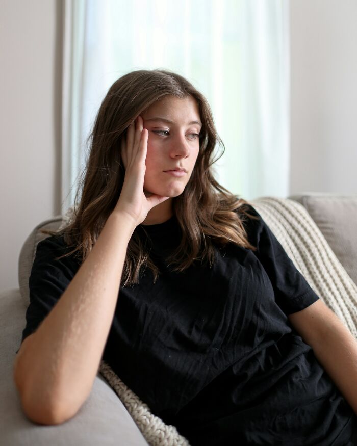 Young woman in black shirt sitting on a couch, looking thoughtful and reflective about marriage realities.