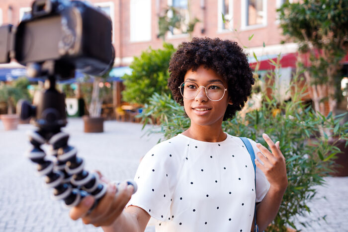 Young woman with glasses recording a vlog outdoors, discussing powerful water dangers and safety awareness.