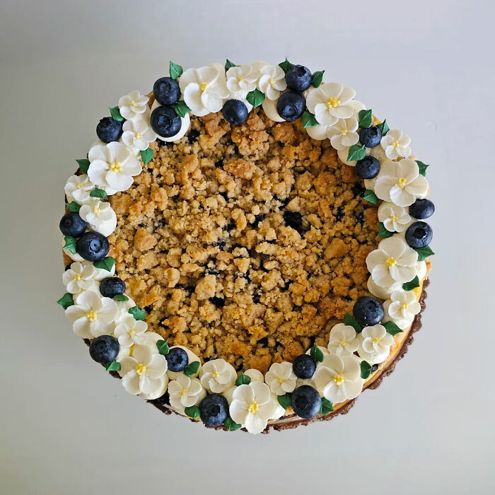 Blueberry crumb cake decorated with white frosting flowers and fresh blueberries showcasing gorgeous baked goods.