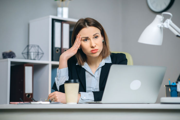 Female software developer looking frustrated at her laptop during a client meeting, highlighting workplace gender bias. Female software developer looking frustrated at her laptop during a client meeting, highlighting workplace gender bias.